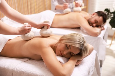 Couple receiving relaxing massage with herbal bags in spa salon, selective focus