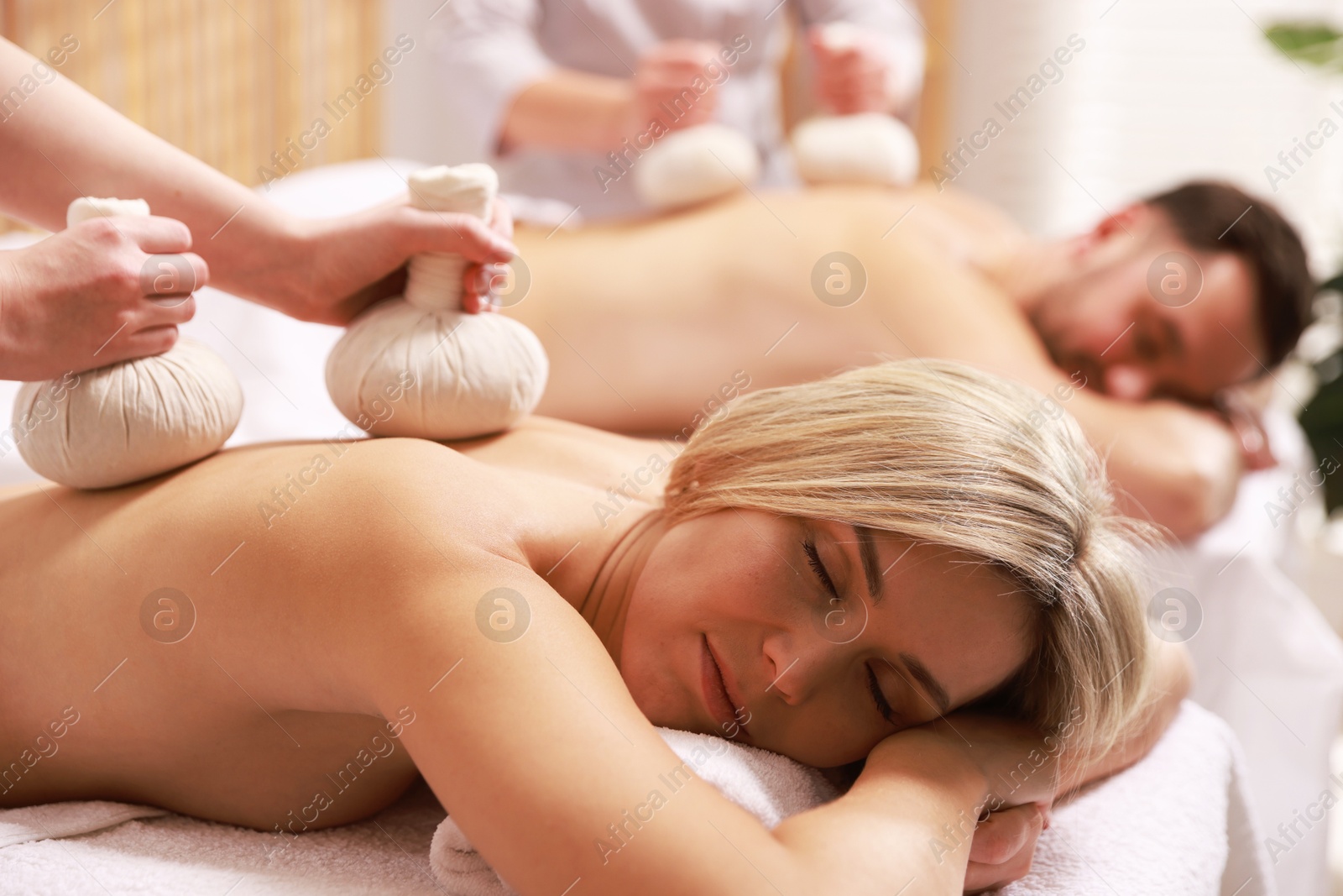 Photo of Couple receiving relaxing massage with herbal bags in spa salon, selective focus