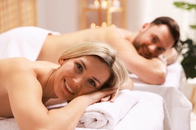 Photo of Happy couple lying on massage tables in spa salon, selective focus