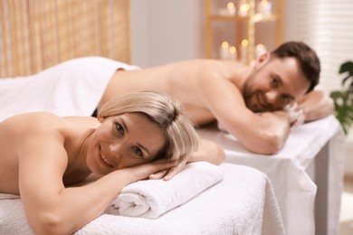 Photo of Happy couple lying on massage tables in spa salon, selective focus