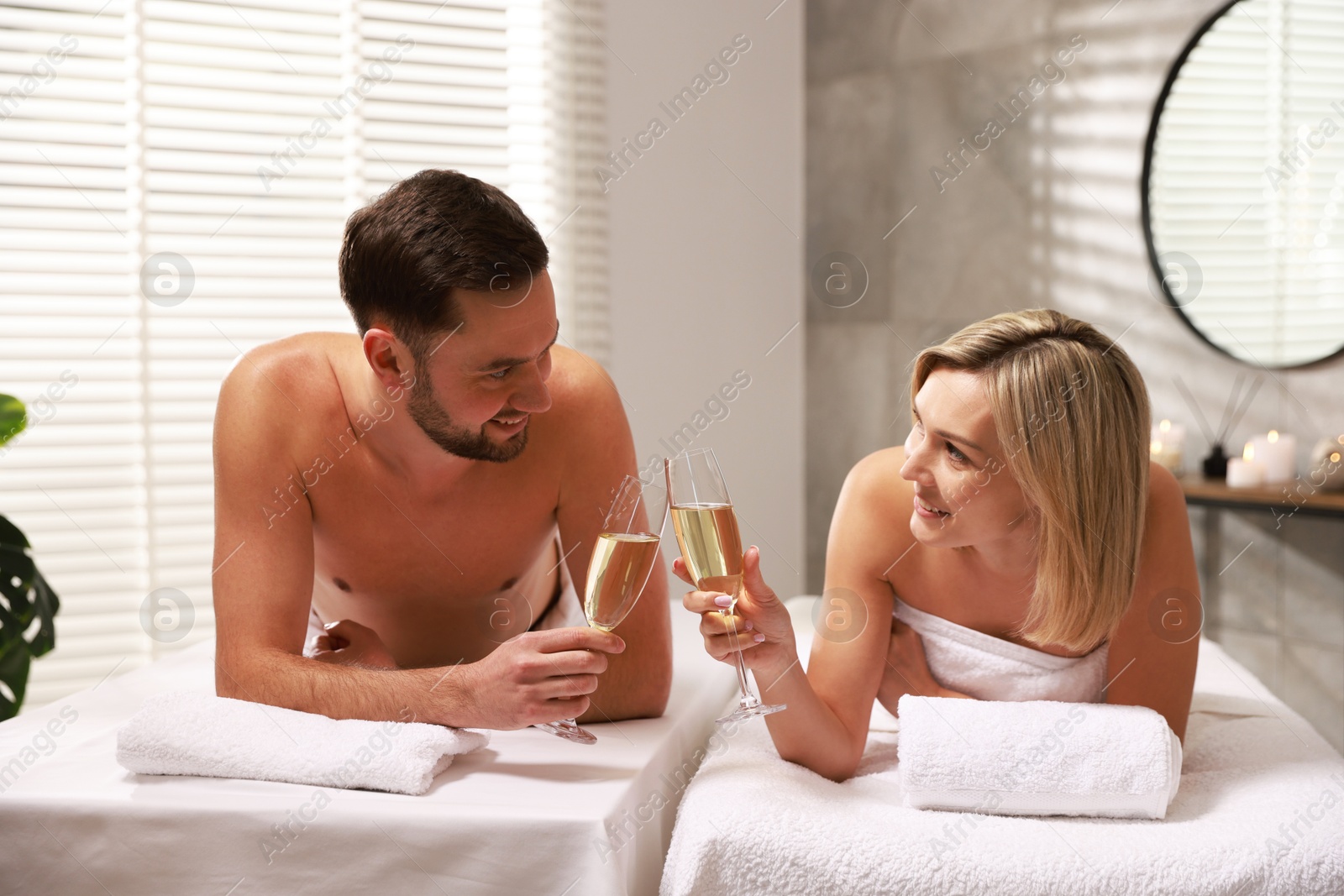 Photo of Happy couple with glasses of champagne lying on massage tables in spa salon