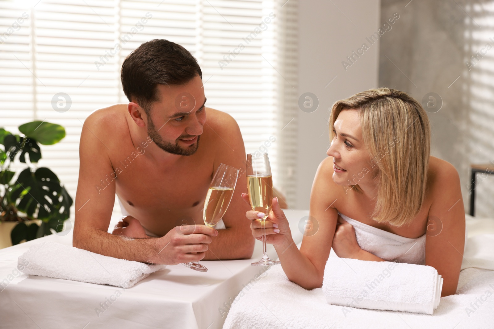 Photo of Happy couple with glasses of champagne lying on massage tables in spa salon