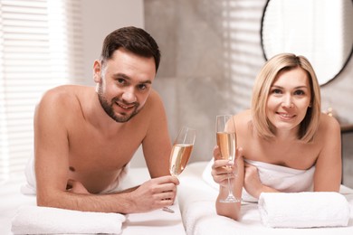 Photo of Happy couple with glasses of champagne lying on massage tables in spa salon