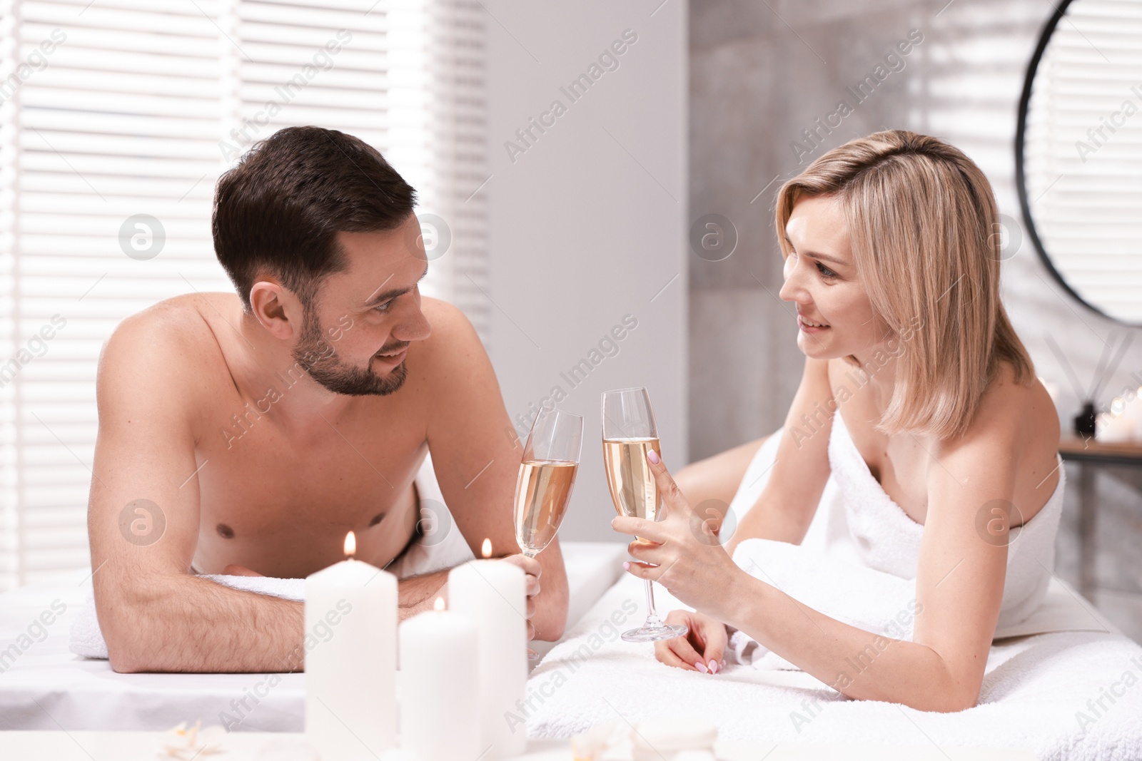 Photo of Happy couple with glasses of champagne lying on massage tables in spa salon