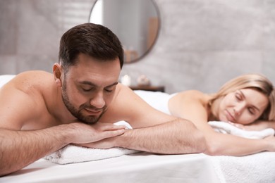 Photo of Couple lying on massage tables in spa salon, selective focus