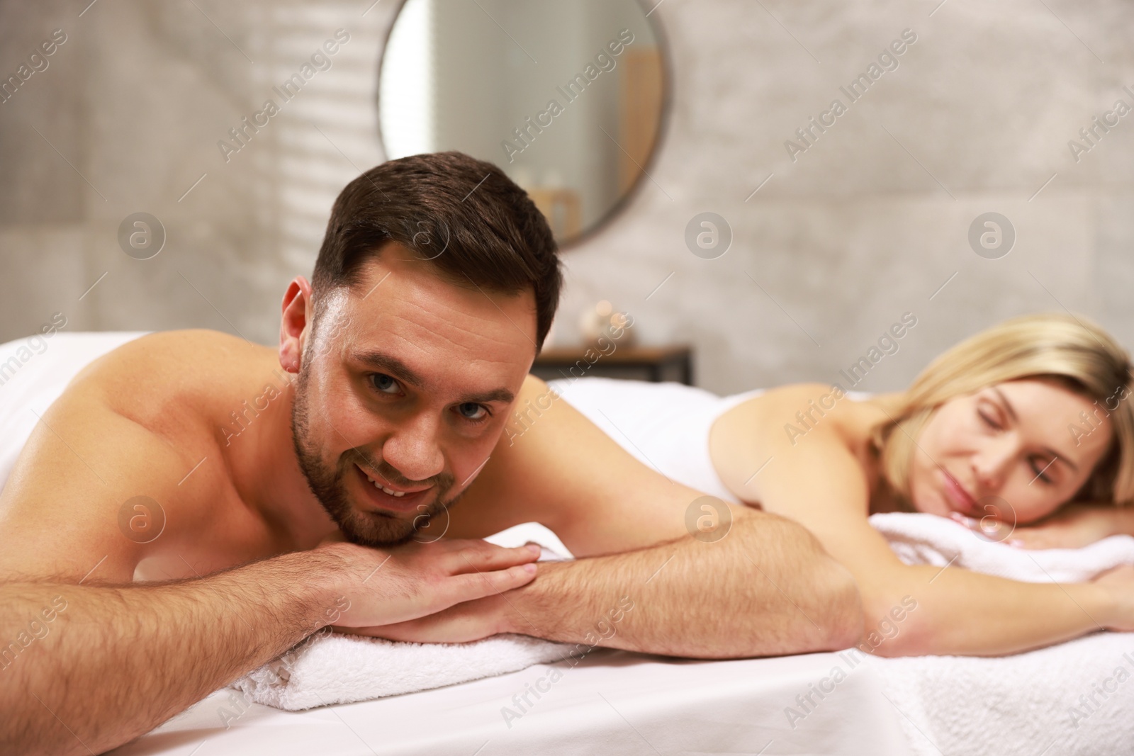 Photo of Happy couple lying on massage tables in spa salon, selective focus