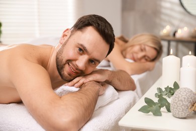 Photo of Happy couple lying on massage tables in spa salon, selective focus