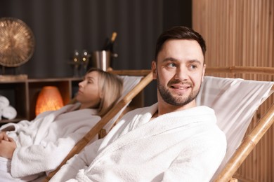 Photo of Happy couple in bathrobes relaxing in spa salon, selective focus