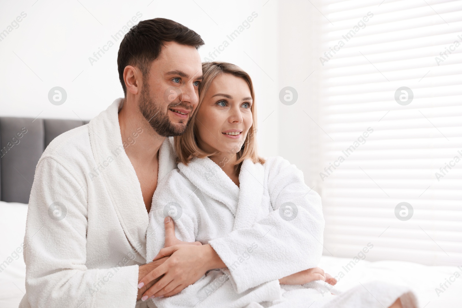 Photo of Spa. Happy couple in bathrobes sitting on bed indoors, space for text