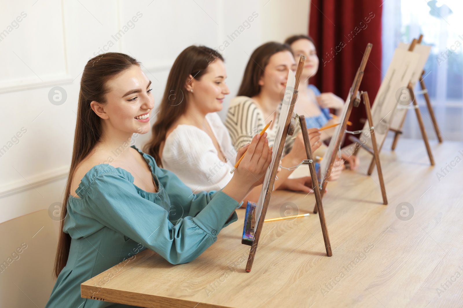 Photo of Group of women with easels learning to draw pictures at wooden table indoors