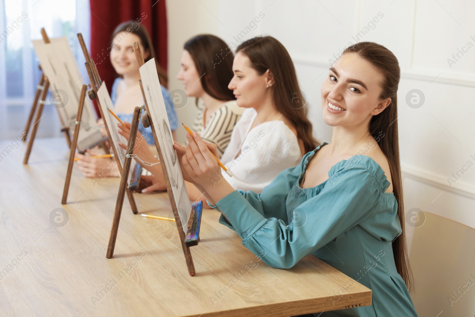 Photo of Group of women with easels learning to draw pictures at wooden table indoors