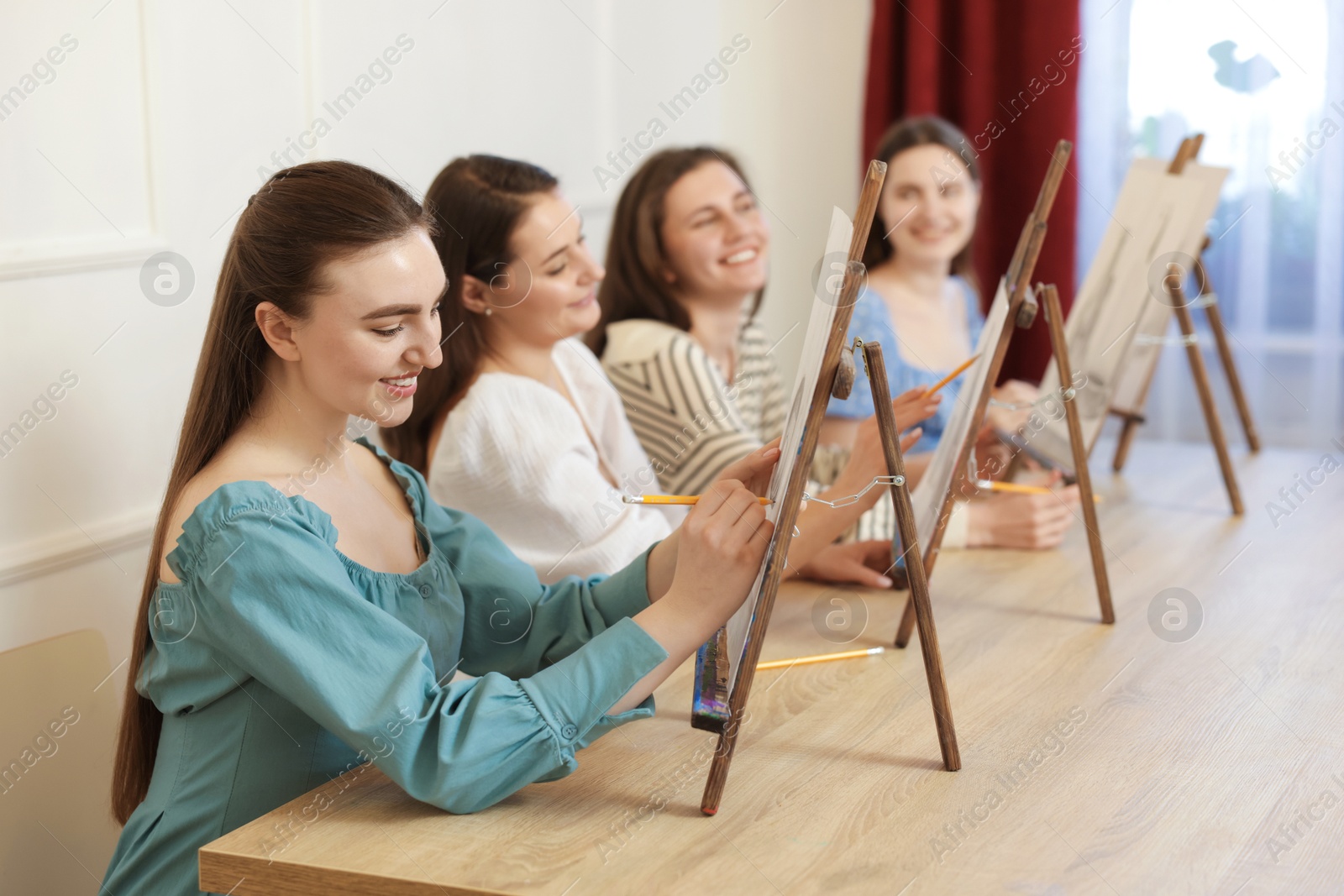 Photo of Group of women with easels learning to draw pictures at wooden table indoors