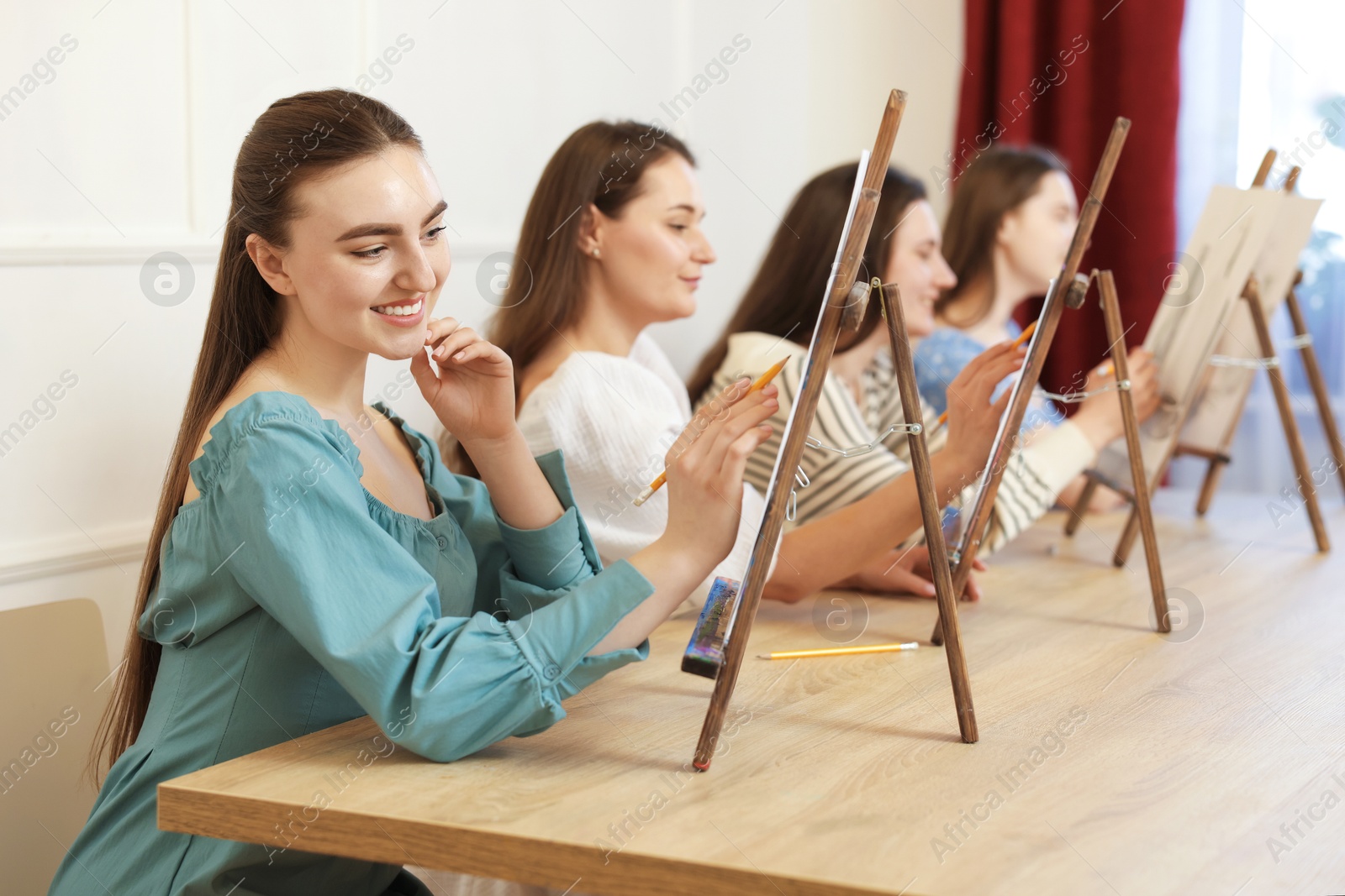 Photo of Group of women with easels learning to draw pictures at wooden table indoors