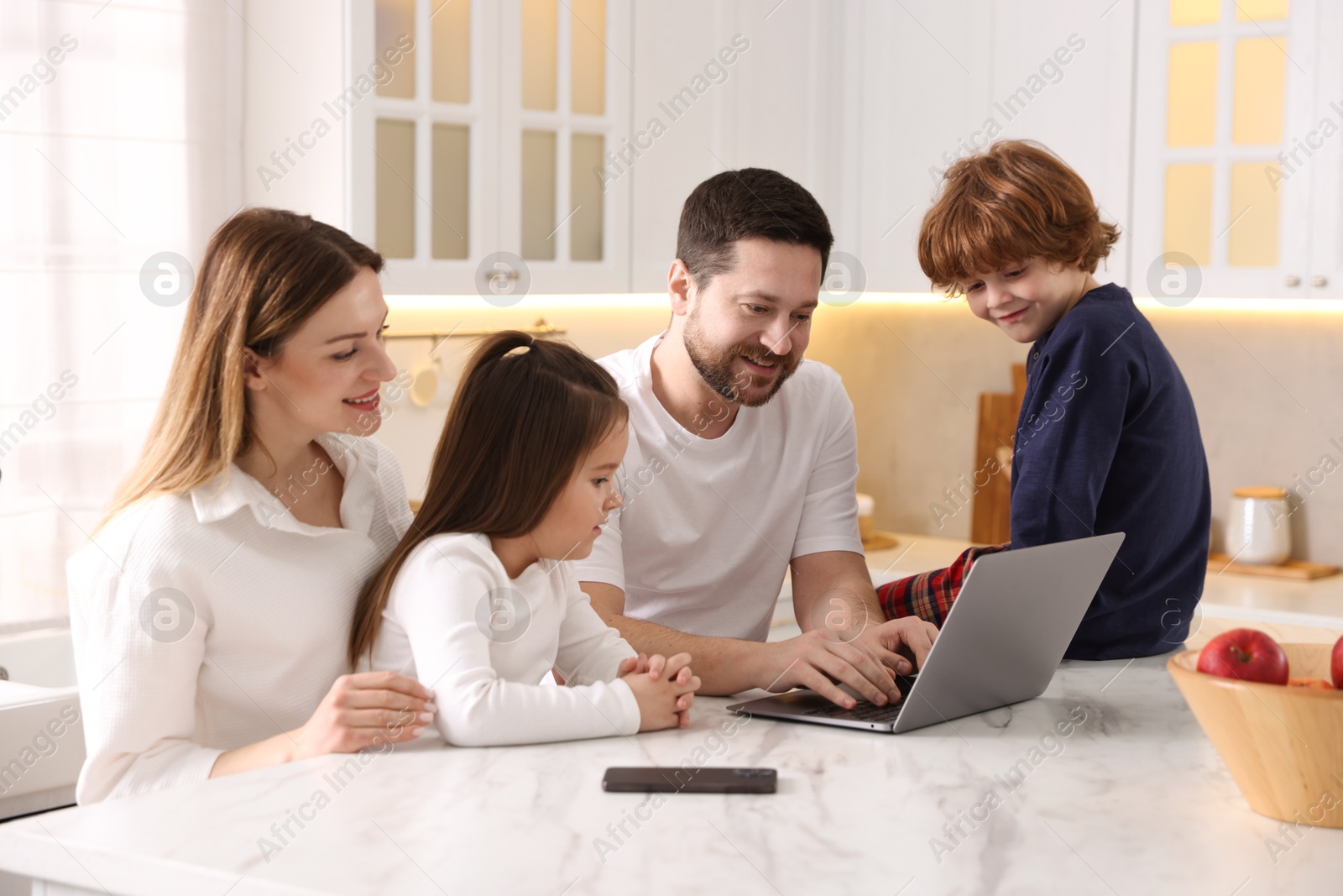 Photo of Happy family wearing stylish pajamas looking at laptop at white marble table in kitchen