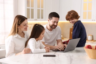 Happy family wearing stylish pajamas looking at laptop at white marble table in kitchen