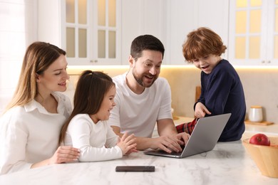 Photo of Happy family wearing stylish pajamas looking at laptop at white marble table in kitchen