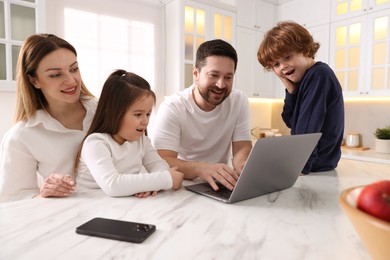 Happy family wearing stylish pajamas looking at laptop at white marble table in kitchen