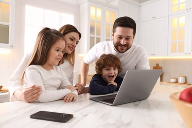 Happy family wearing stylish pajamas looking at laptop at white marble table in kitchen