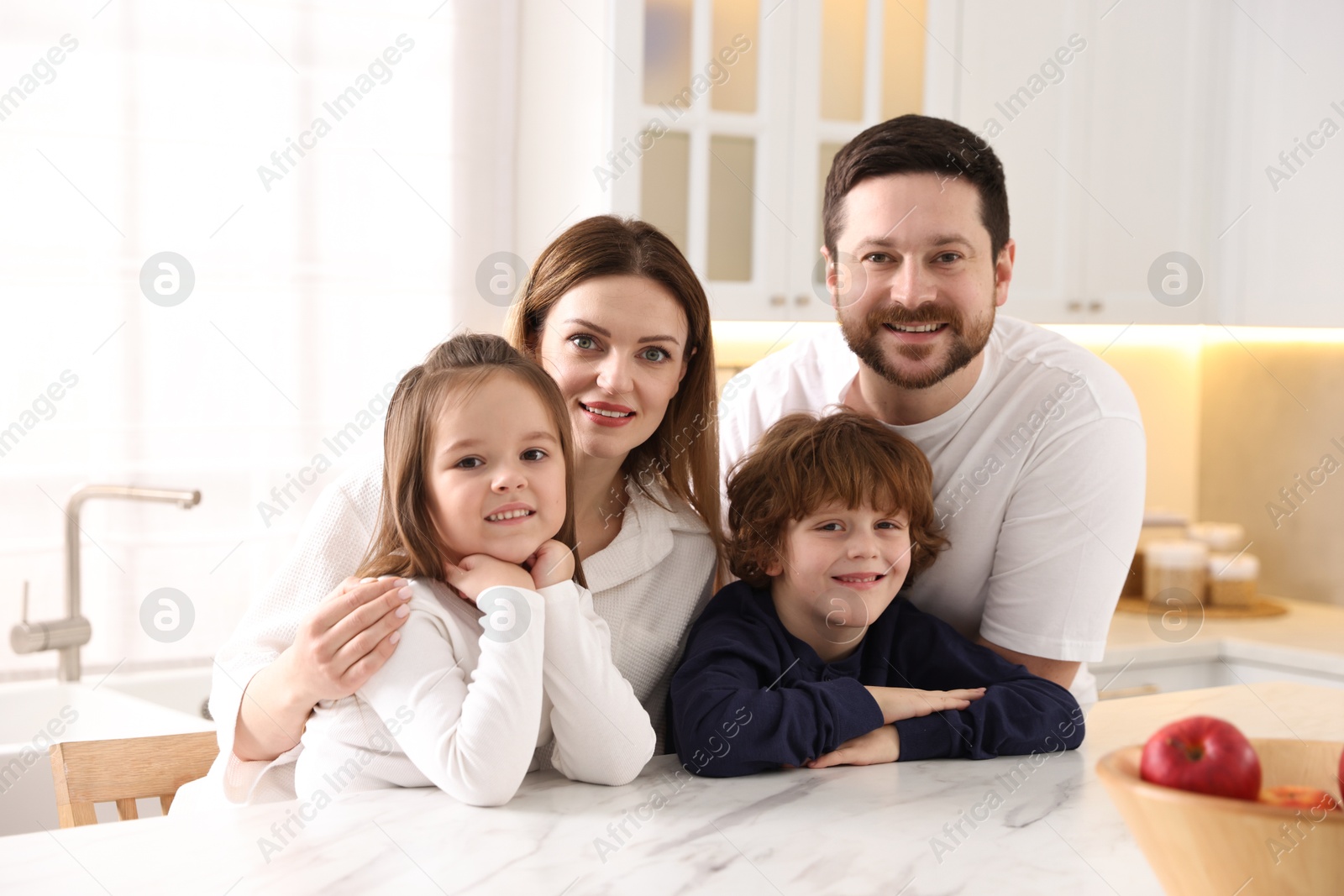 Photo of Family portrait of happy parents and their children wearing stylish pajamas at white marble table in kitchen