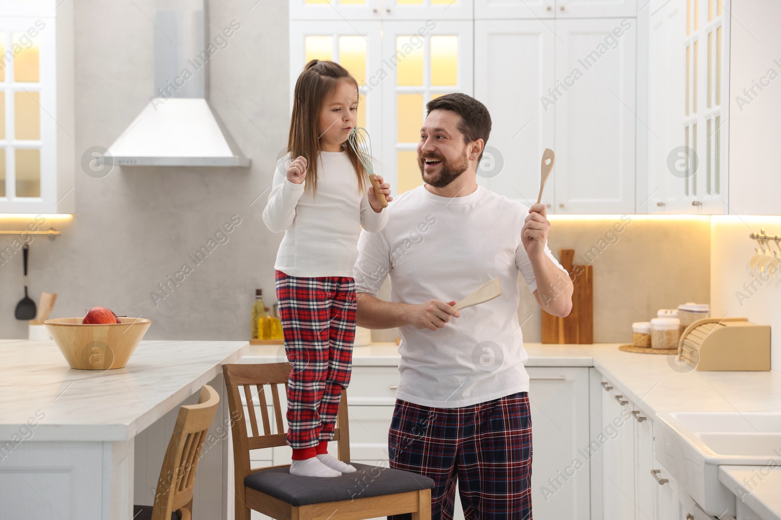 Photo of Happy father and his daughter wearing stylish pajamas having fun with cookware in kitchen