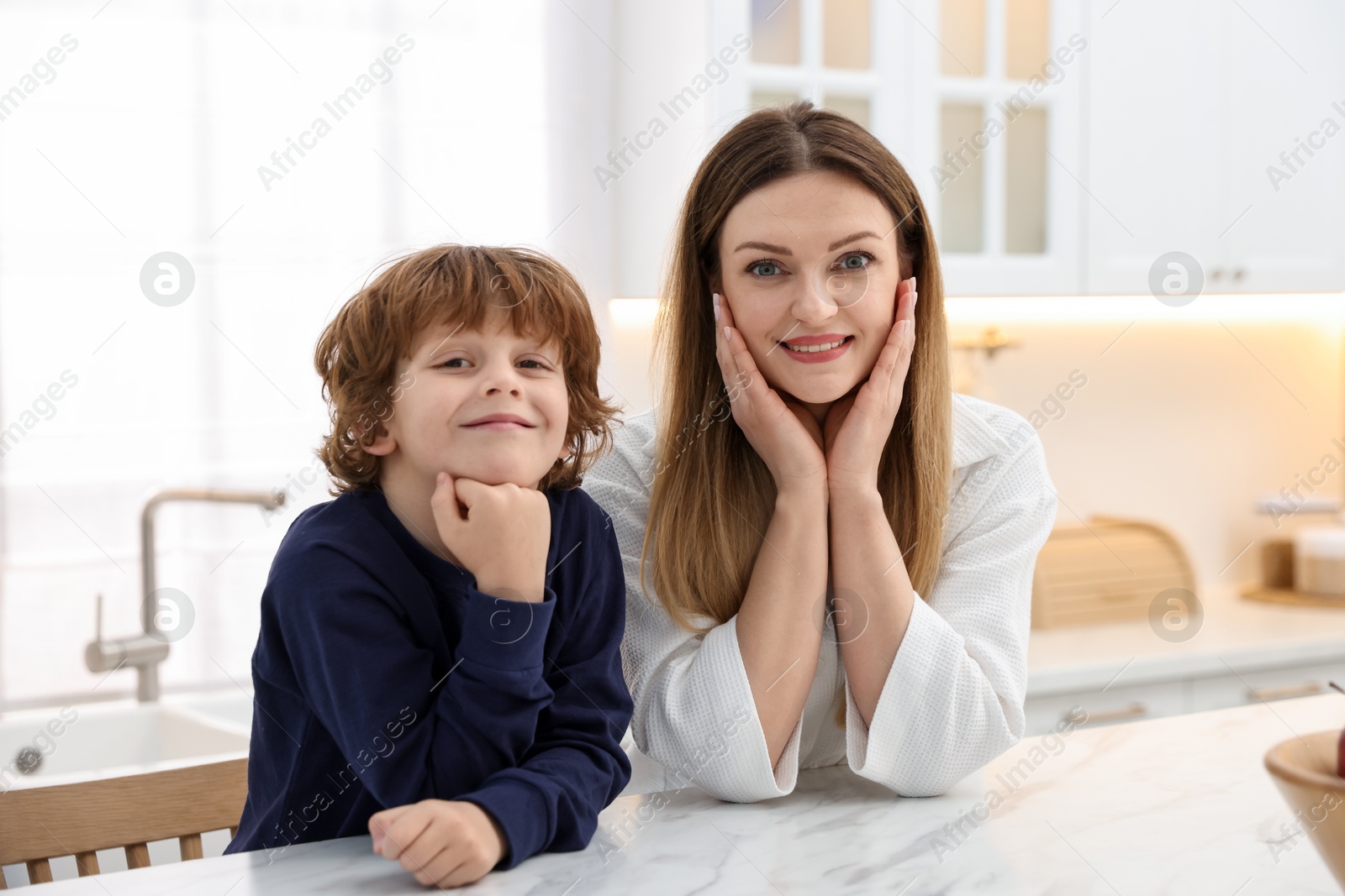 Photo of Family portrait of smiling woman and her son wearing stylish pajamas at white marble table in kitchen