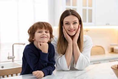 Family portrait of smiling woman and her son wearing stylish pajamas at white marble table in kitchen