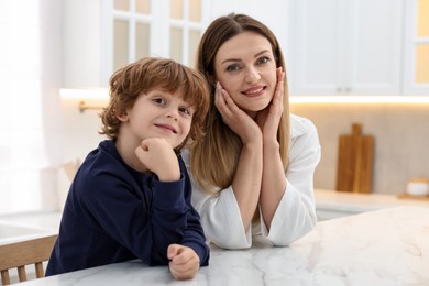 Family portrait of smiling woman and her son wearing stylish pajamas at white marble table in kitchen