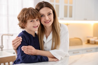 Photo of Family portrait of smiling woman and her son wearing stylish pajamas at table in kitchen