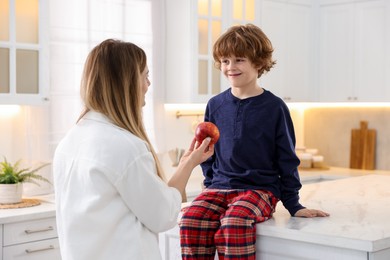 Photo of Woman and her son wearing stylish pajamas spending time together in kitchen