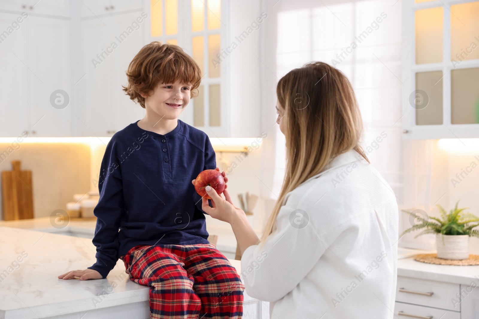 Photo of Woman and her son wearing stylish pajamas spending time together in kitchen