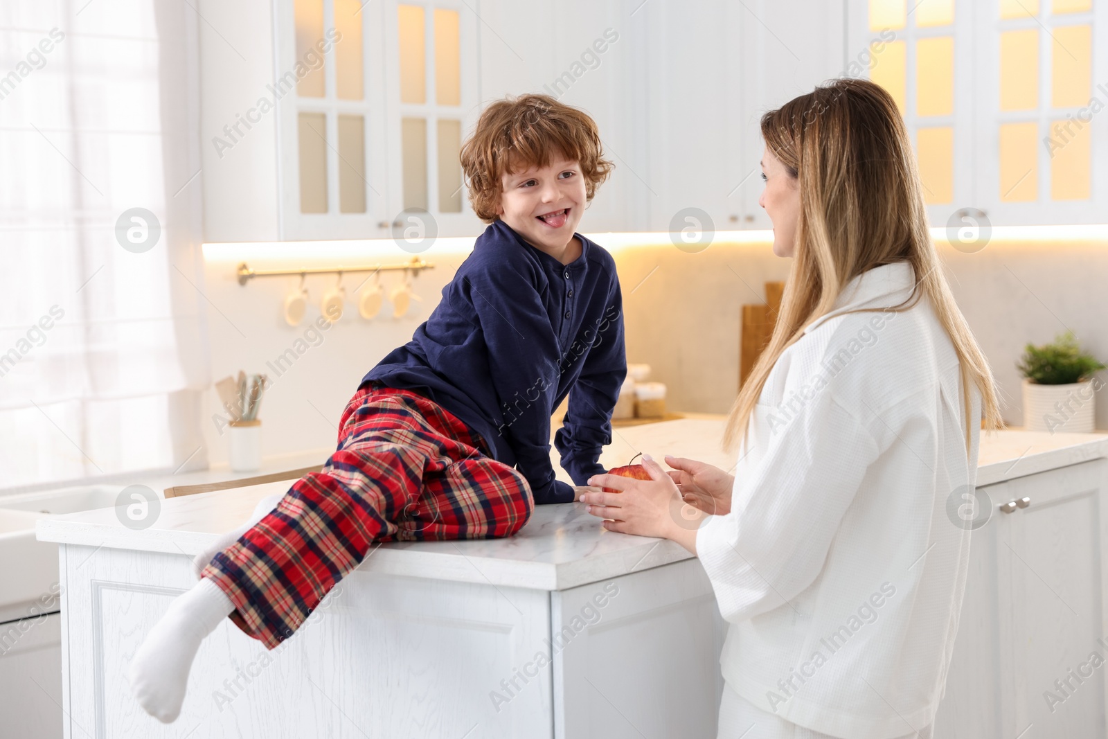 Photo of Woman and her son wearing stylish pajamas spending time together in kitchen