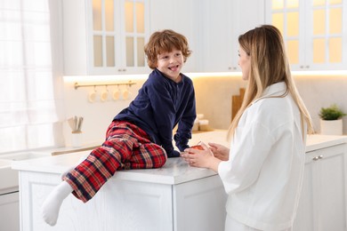 Photo of Woman and her son wearing stylish pajamas spending time together in kitchen