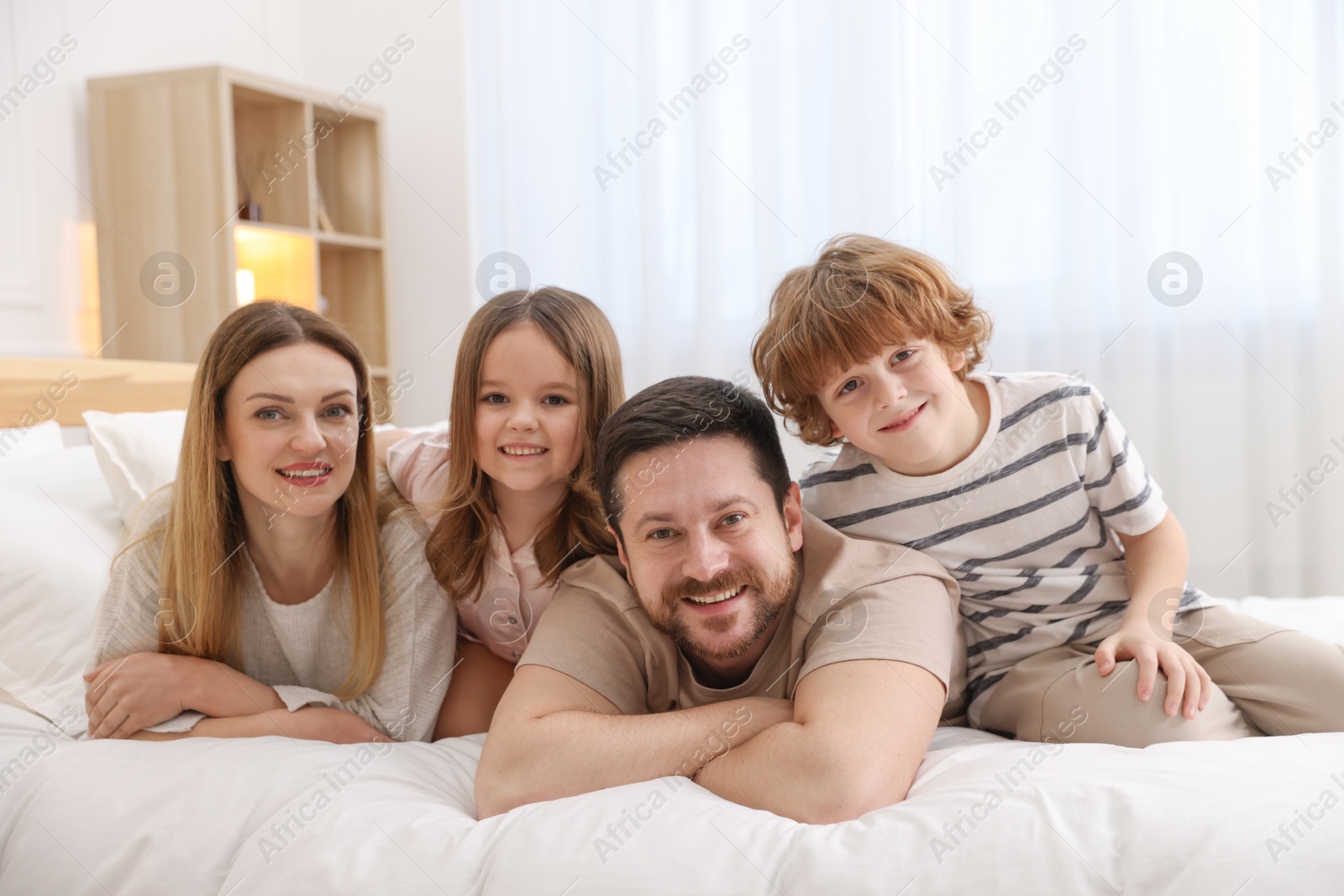 Photo of Family portrait of happy parents and their children wearing pajamas on bed at home