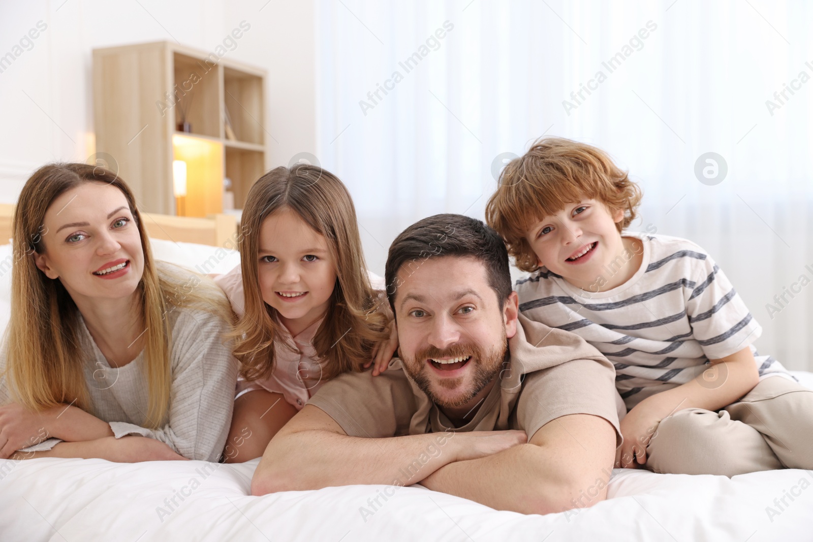 Photo of Family portrait of happy parents and their children wearing pajamas on bed at home