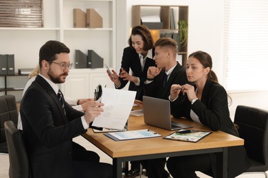 Photo of Coworkers working together at wooden table in office