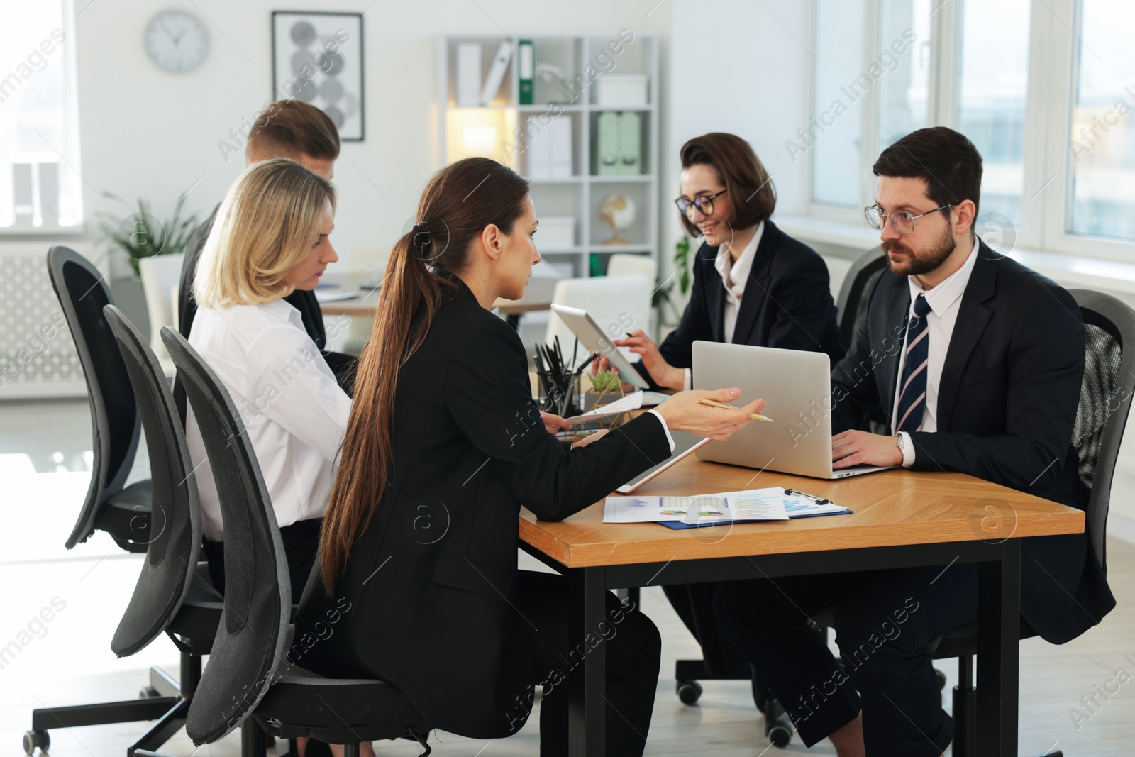 Photo of Coworkers with different devices working together at wooden table in office