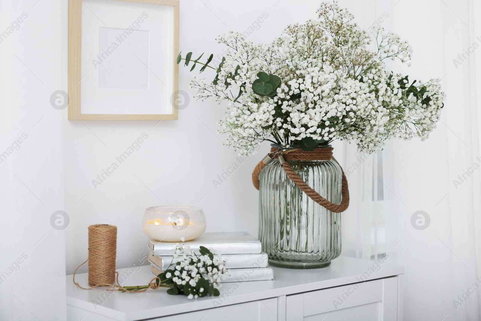 Bouquet of beautiful gypsophila flowers and eucalyptus branches in vase near decorative elements on chest of drawers indoors Photo of Bouquet of beautiful gypsophila flowers and eucalyptus branches in vase near decorative elements on chest of drawers indoors