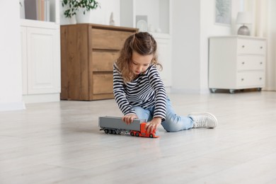 Photo of Little girl playing with toy car on floor at home