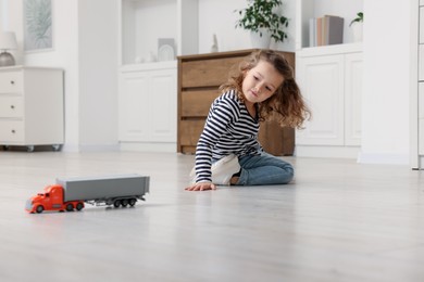 Photo of Little girl playing with toy car on floor at home