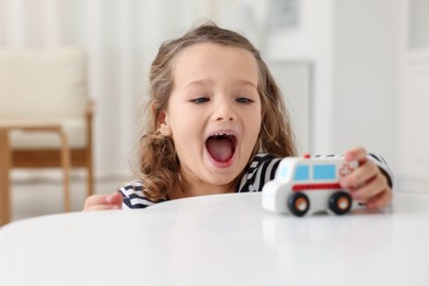 Photo of Little girl playing with toy car at white table indoors