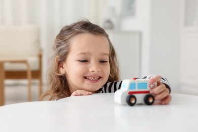 Photo of Little girl playing with toy car at white table indoors