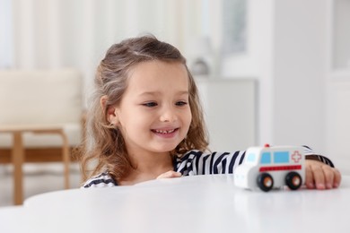 Photo of Little girl playing with toy car at white table indoors