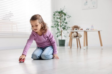 Photo of Little girl playing with toy car on floor at home, space for text