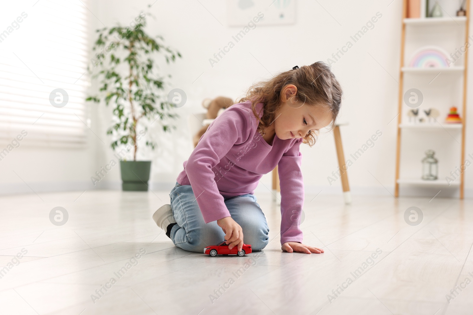 Photo of Little girl playing with toy car on floor at home