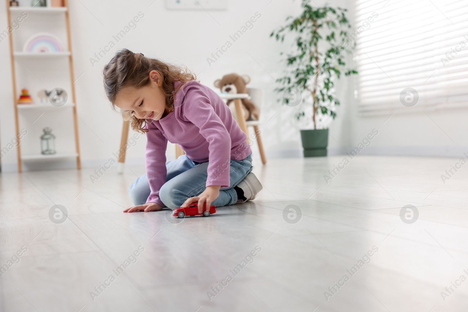 Photo of Little girl playing with toy car on floor at home, space for text