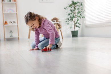 Photo of Little girl playing with toy car on floor at home, space for text