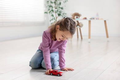 Photo of Little girl playing with toy car on floor at home