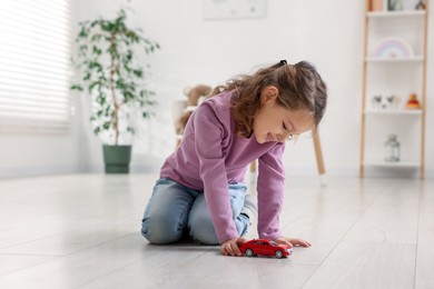 Photo of Little girl playing with toy car on floor at home