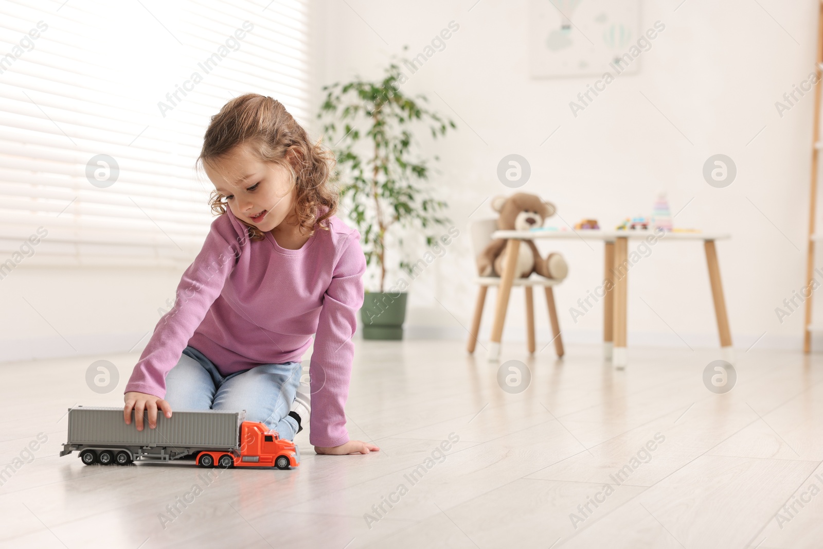 Photo of Little girl playing with toy car on floor at home, space for text