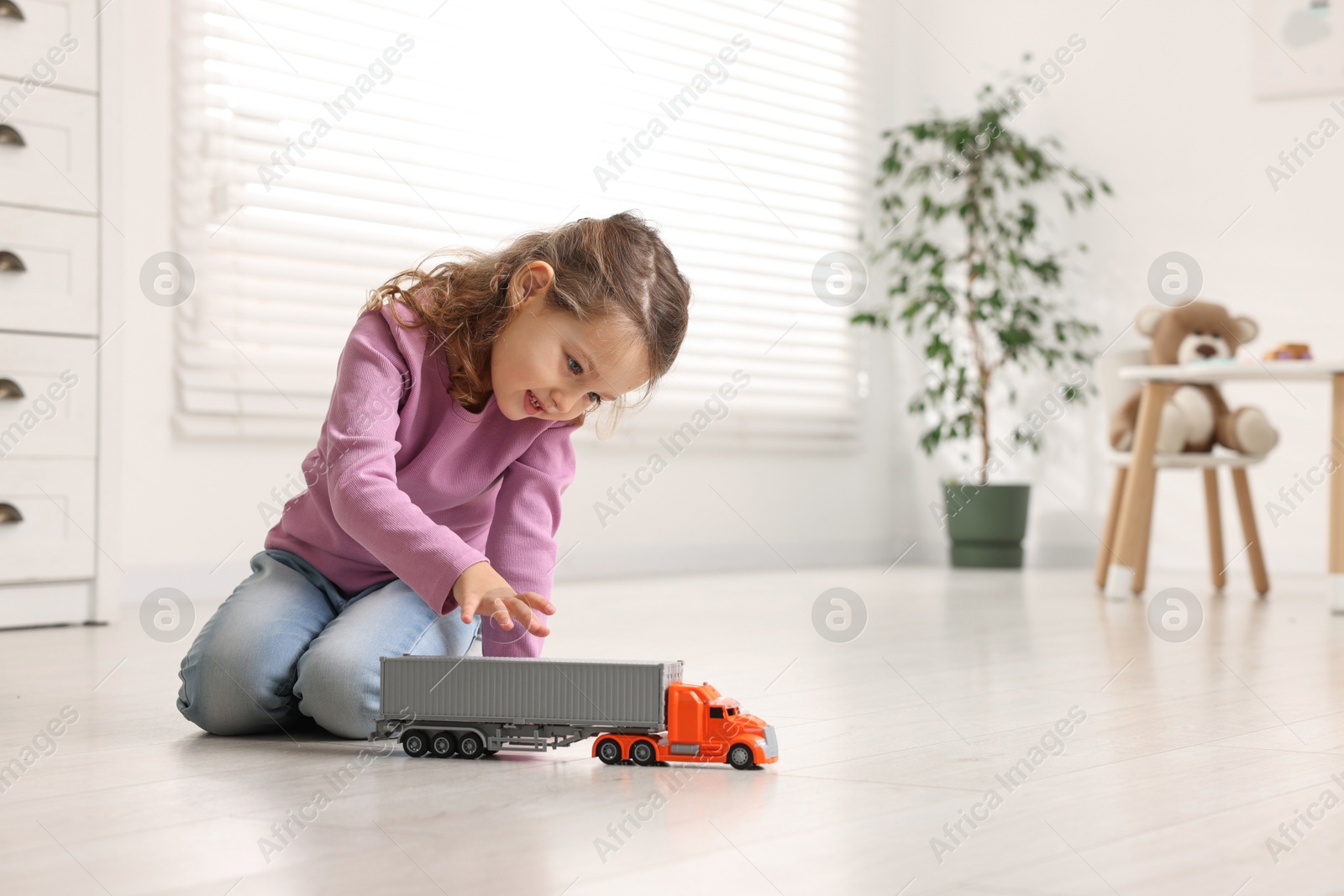 Photo of Little girl playing with toy car on floor at home, space for text